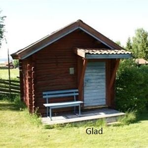 Stuga Glad är en röd liten timmerstuga med blå dörr och en blå bänk bredvid dörren. 