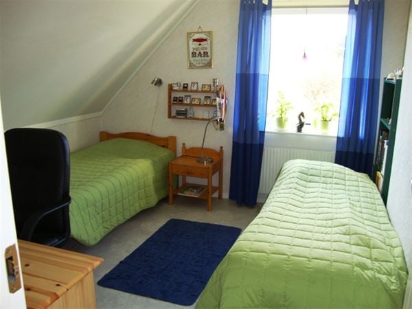 Two single beds with green bedspread and blue curtains.  