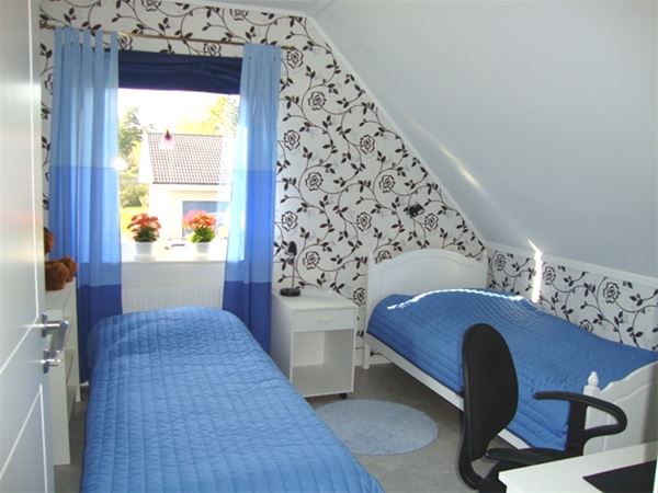 Två enkelsängar i ett rum med blå gardiner och svart- och vitblommig tapet. 