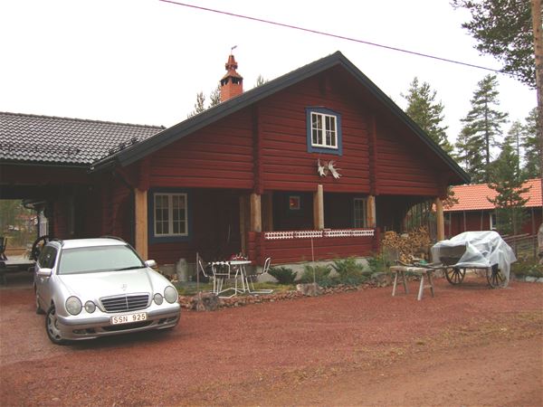 Exteriör av rödmålat hus med stor veranda. 
