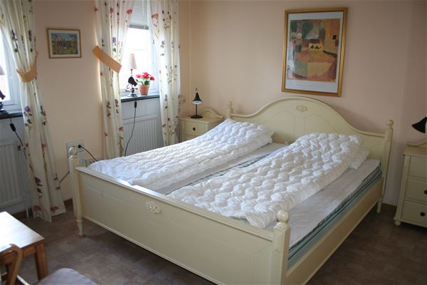 Dubbelsäng i en vit sängram och vita nattduksbord i ett rum med beige vägg. 