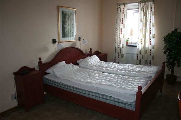 Double bed in a dark brown, wooden bed frame with matching chest of drawers besife.  