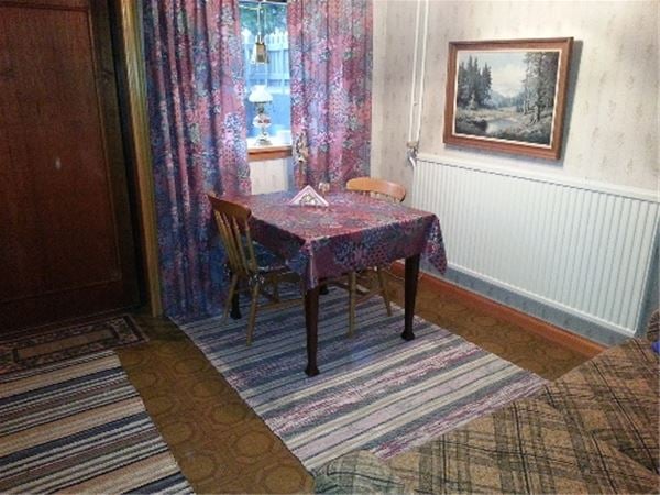 Matbord med två stolar framför ett fönster med lila, mönstrad gardin med matchande vaxduk.  