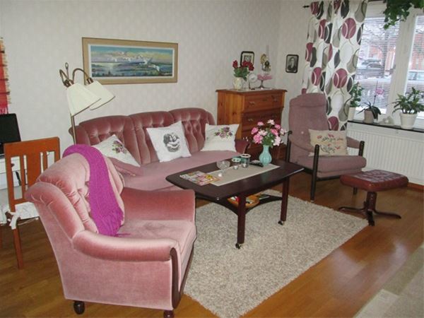 Vardagsrum med rosa soffa och fåtöljer framför tv. 