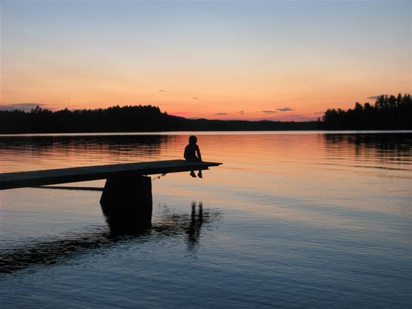 Solnedgång vid sjö med siluett av barn på brygga.  