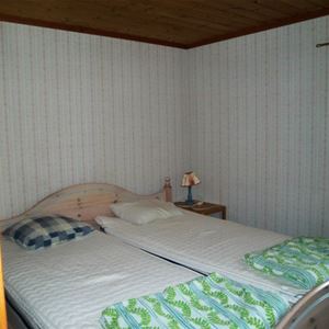 Dubbelsäng i sängram i ett rum med vita randig tapeter. 