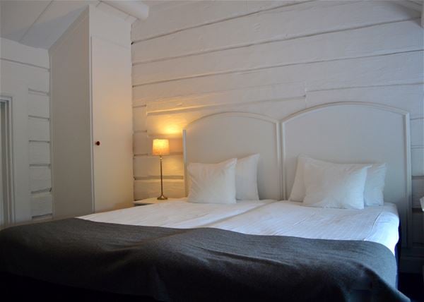 Double bed with white headboard against a white painted wooden wall. 