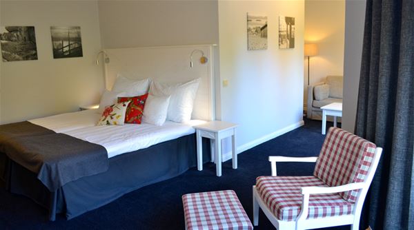 Ett rum med en säng med vit sänggavel och en rödrutig fåtölj. 