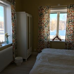 Sovrum med mönstrade gardiner med dala-motiv, vita sängkläder och vit garderob med spegeldörrar.