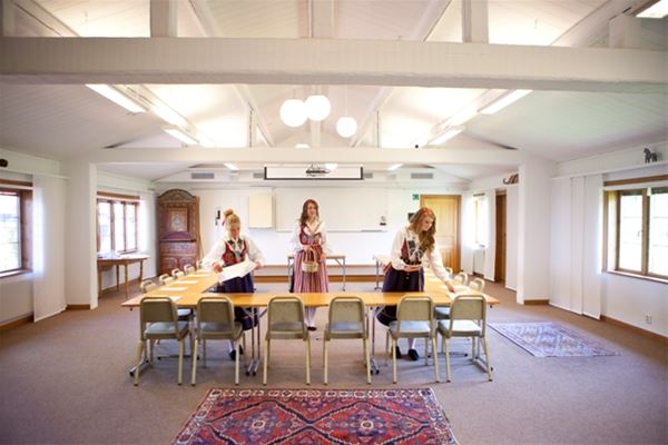Three women in folklore costumes are preparing for a conferense in a bright room with several windows.  