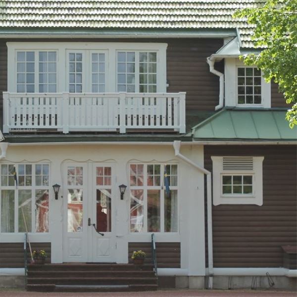 Entrén på Trunna Vandrarhem och konferens med vit dubbeldörr, spröjsade fönster och balkong med vitt räcke.  
