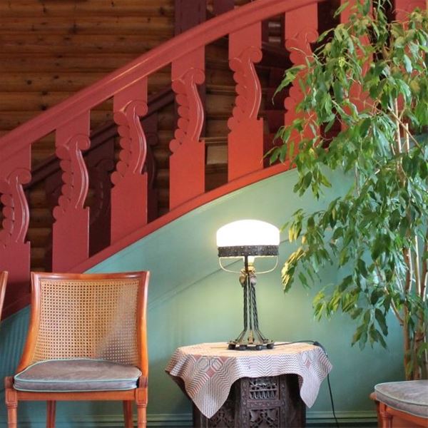 Detalj på rödmålat trappräcke med en stol och ett litet bord med lampa framför. 