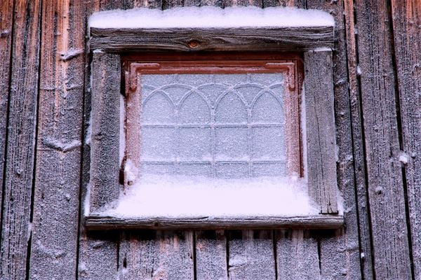 Blyinfattat förnster som har frost på rutan och snö på fönsterbläcket.  
