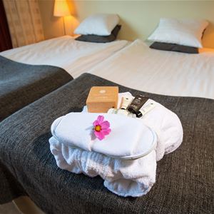 Spakit med morgonrock, tofflor, rosa blomma och hygienartiklar ligger på en säng. 
