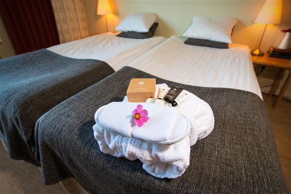 Spakit med morgonrock, tofflor, rosa blomma och hygienartiklar ligger på en säng.  