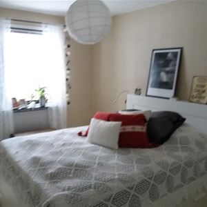 Double bed with a white headboard in a bright room with white curtains in the window. 