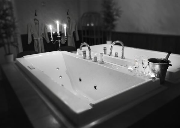 Whirlpool tub with candles and two glasses of wine standing on the bathtub edge.  