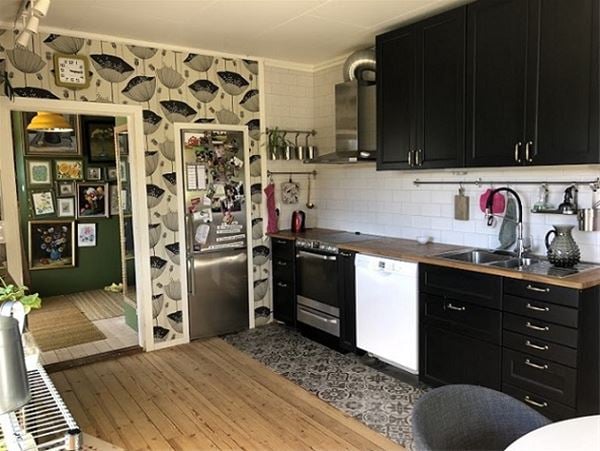 Kitchen with black cupboards and patterned wallpaper in black, grey and white. 