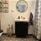 Ett badrum med vitt kakel, grått, mönstrat klinkers, toalett och en svart kommod med en rund spegel ovanför.