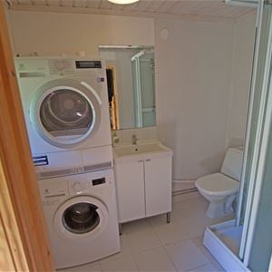 Badrum med tvättmaskin, torktumlare, duschkabin, toalett och handfat.