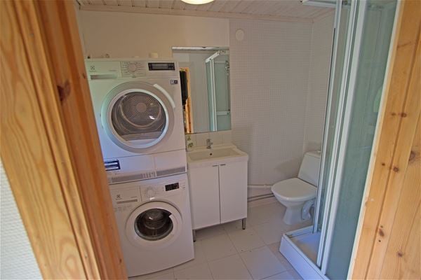 Bathroom with washing machine, dryer, shower cabin, toilet and sink.  
