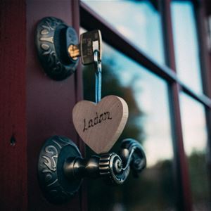 Detalj på dörrhandtag med nyckel i dörren och ett hjärta av trä som nyckelring.
