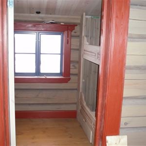 Detail of inside timber walls, a gray bunkbed and red door and window linings. 