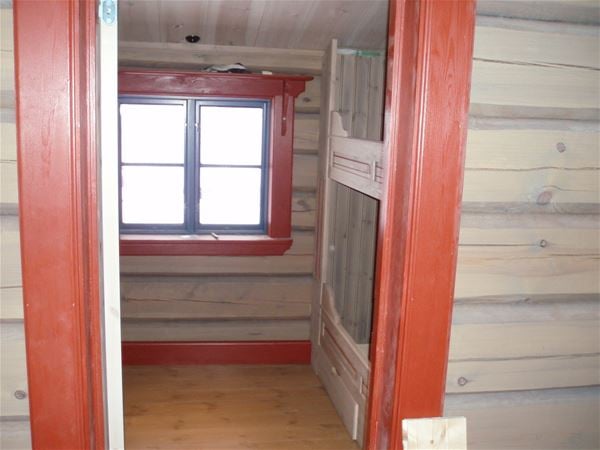 Detail of inside timber walls, a gray bunkbed and red door and window linings.  