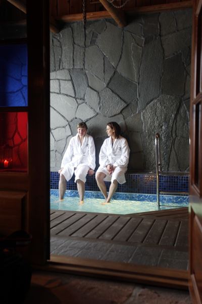 Two persons are sitting on the edge of the indoor pool.  