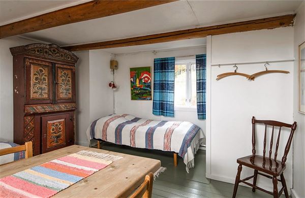 Rum med gammalt skåp med dalmålningar, en enkelsäng, en pinnstol och ett matbord.  