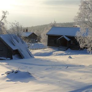 Två timmerhus på ett gårdstun en solig vinterdag.