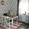 Matbord med 3 vita stolar i ett kök med en tapet med grått blom-mönster och gråa gardiner. 