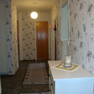 Hall with white chest of drawers with a candle and carpets in bright grey on dark grey floor. 
