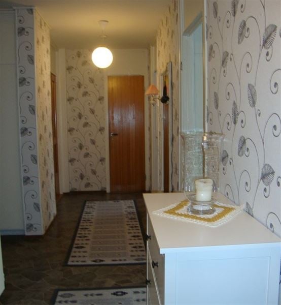 Hall with white chest of drawers with a candle and carpets in bright grey on dark grey floor.  