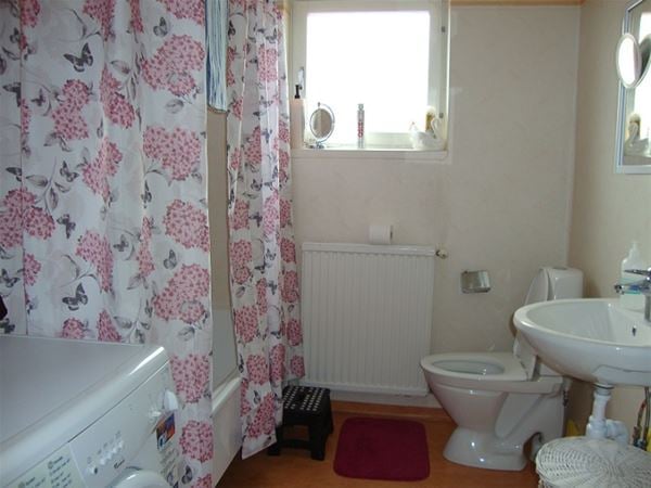 Badrum med toalett, handfat och ett badkar bakom ett rosa-blommigt duschdraperi.  