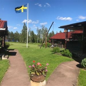 Flowers in a flowerpot in front of a flagpole with a swedish flag blowing in the wind. 
