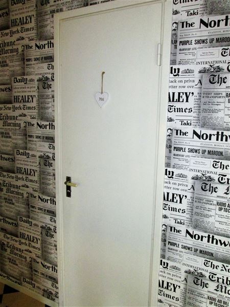 Toalettdörr i en hall med tapet som ser ut som gamla  dagstidningar. 