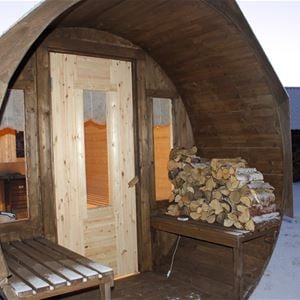 Sauna from outside with wood on the bench beside the door. 