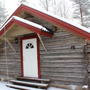 Grey log cabin with white door and snow on the doorstep. 