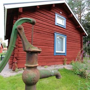 Water pump in front of a red log cabin.