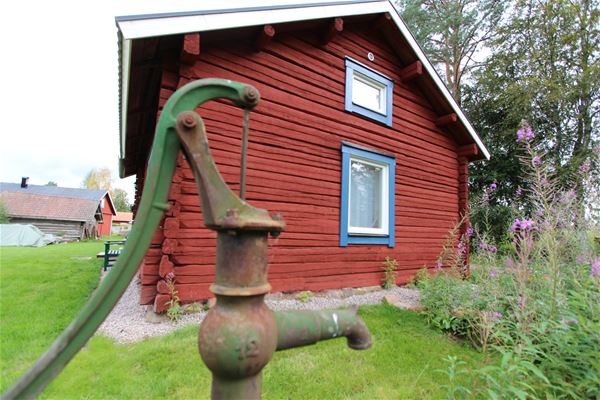 Water pump in front of a red log cabin. 