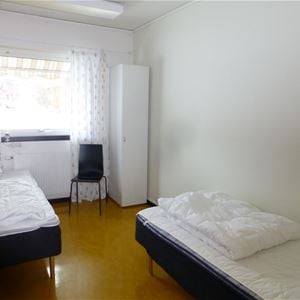 Rum med två enkelsängar på vardera sidan av rummet med ett fönster.