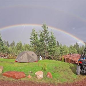 Tält uppställt på gräsmattan med regnbåge i bakgrunden.