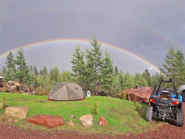 Tält uppställt på gräsmattan med regnbåge i bakgrunden. 