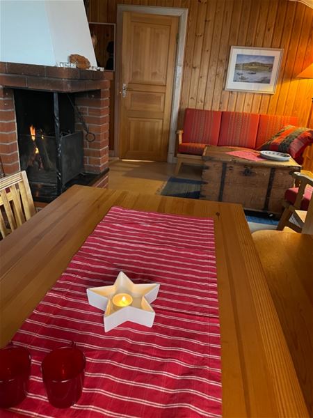 Röd duk på bordet och ett ljus format som en stjärna och en brasa vid soffan i bakgrunden. 