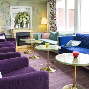 A sofa and violet armcharis and small round tables in the lobby. 