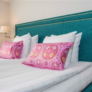 Turkos sänggavel och mönstrade, rosa kuddar på sängen. 