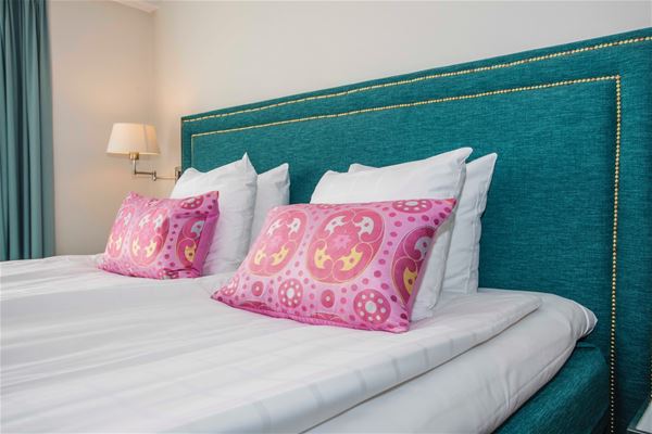 Turkos sänggavel och mönstrade, rosa kuddar på sängen.  