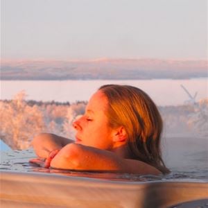 Woman relaxing in the jacuzzi with frost-covered trees and Siljan in the background.