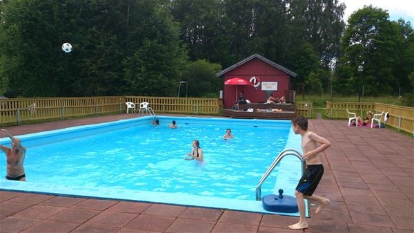 People bathing in an outdoor pool surronded by stone walkways and lawns. 